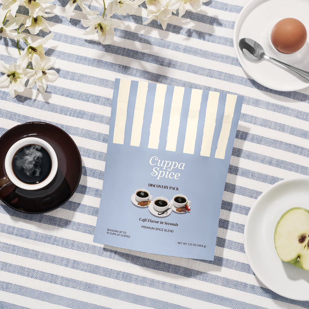 Cuppa Spice coffee seasonings package on a striped tablecloth with a cup of coffee and fruit.