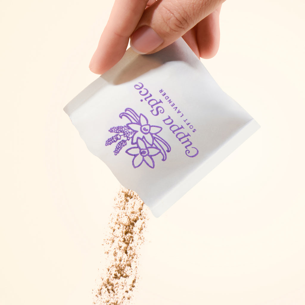 Hand pouring lavender and vanilla spice from a white packet on a beige background