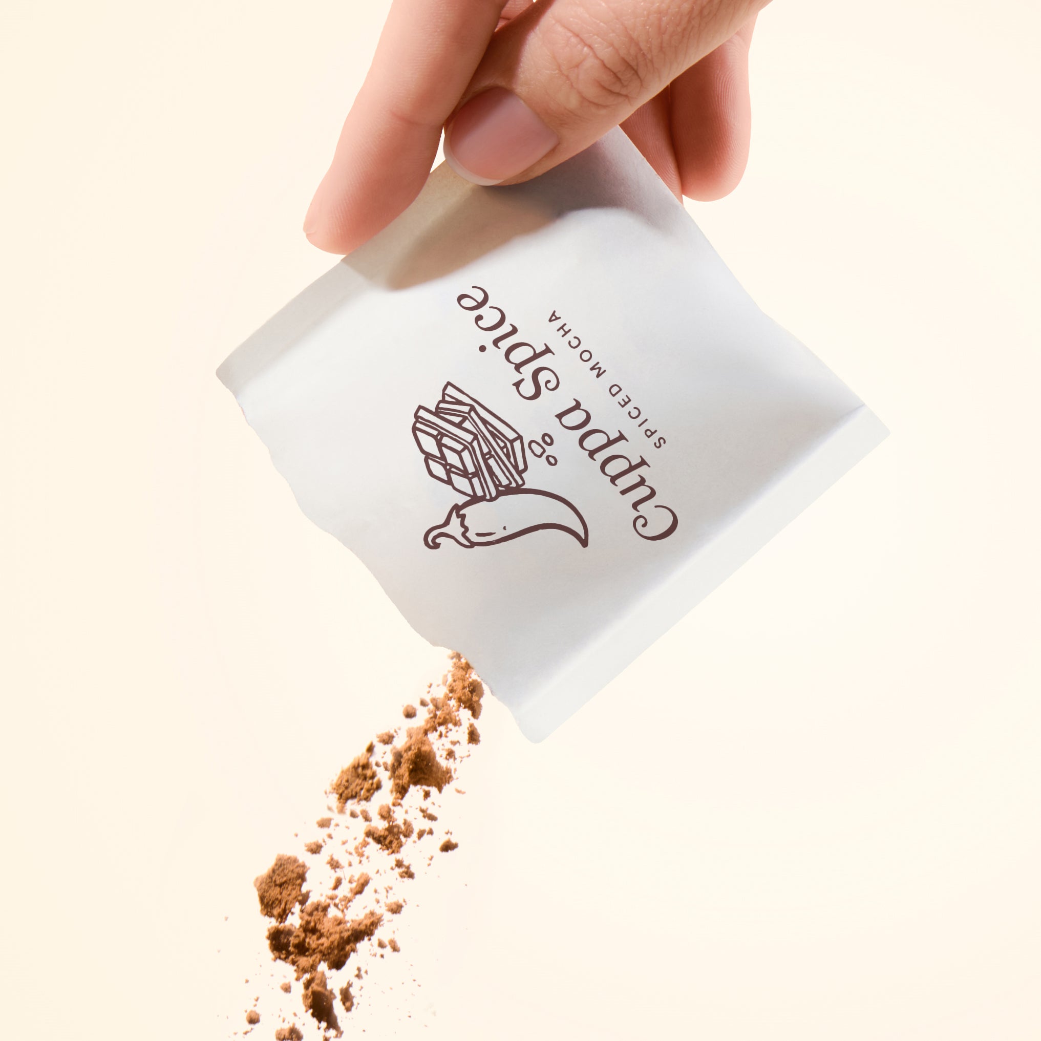 Hand pouring spiced mocha flavor spice from a white packet on a beige background
